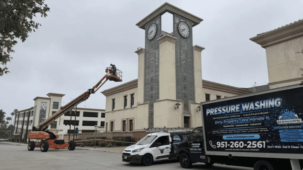 Clock-tower building under maintenance with a worker on a lift cleaning the façade; a pressure-washing van in the foreground.