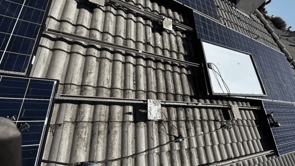 Solar panels mounted on a gray tiled roof with metal rails and visible cabling