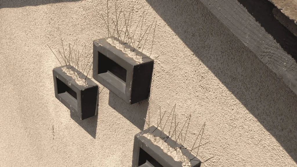 Hollow concrete blocks attached to a rough beige wall with exposed steel reinforcement bars sticking upward, a construction detail.