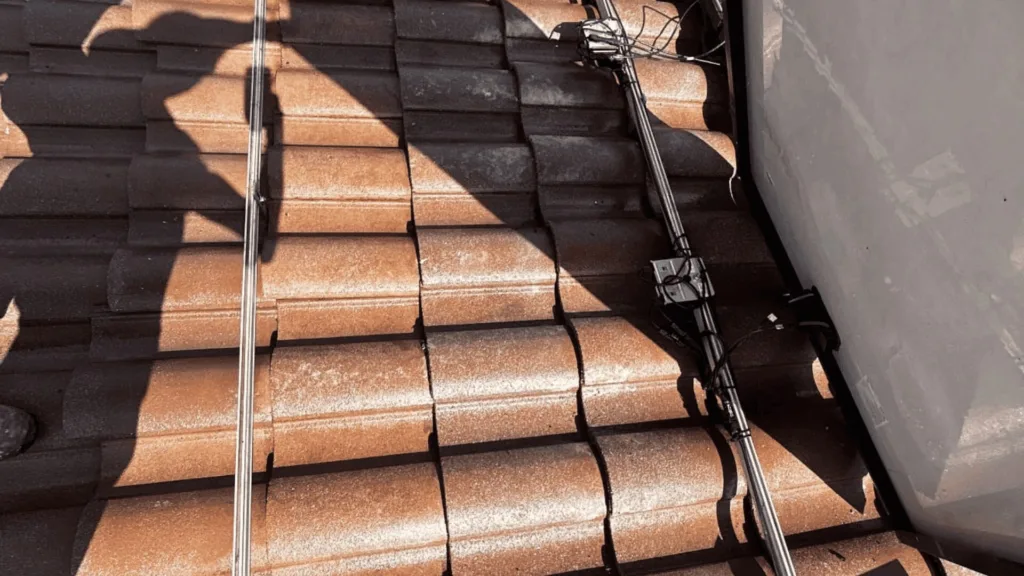 Brown tiled roof with exposed electrical cables and a metal antenna/mast resting on the tiles, casting shadows.