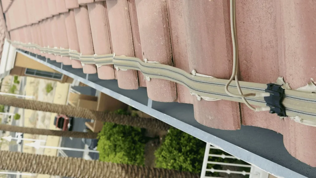 Rooftop edge with red clay tiles and exposed beige electrical cables tied along a rail and a small junction box nearby