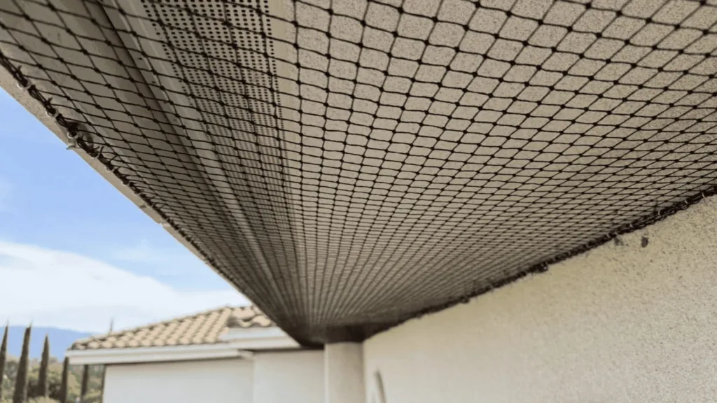 Close-up of black mesh safety netting mounted along a concrete balcony edge, blue sky visible.