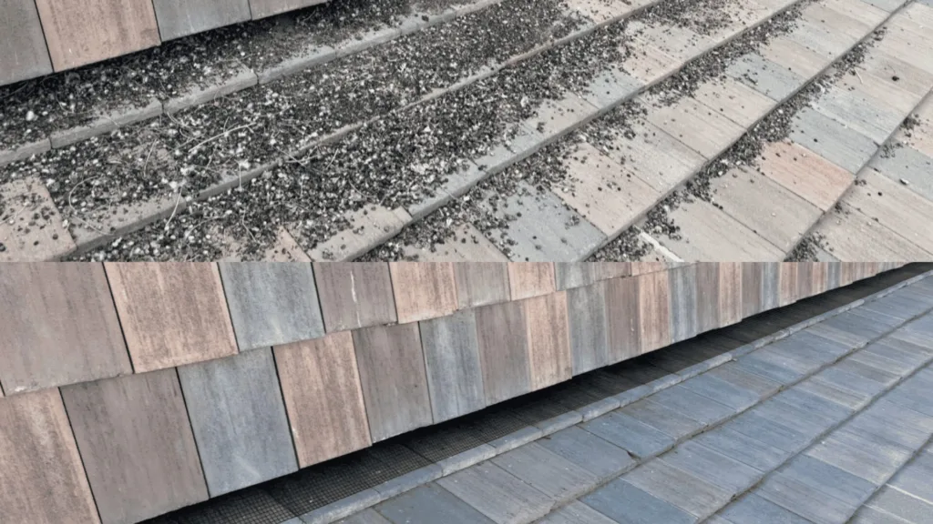 Close-up of a sloped roof with rectangular slate shingles and scattered gravel/debris along the joints and ridges.
