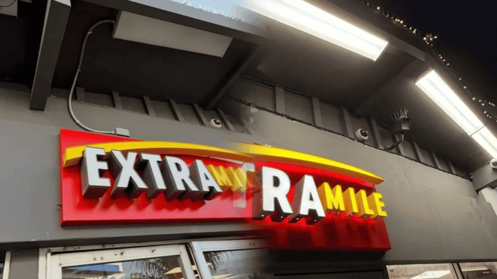 Exterior storefront with a bold red sign reading 'EXTRA RAMBLE' and a yellow curved accent above the text at night.