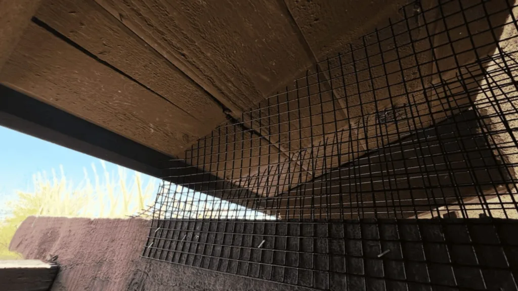 Wire reinforcement mesh leaning against a brown wooden beam at an outdoor construction site under a clear blue sky.