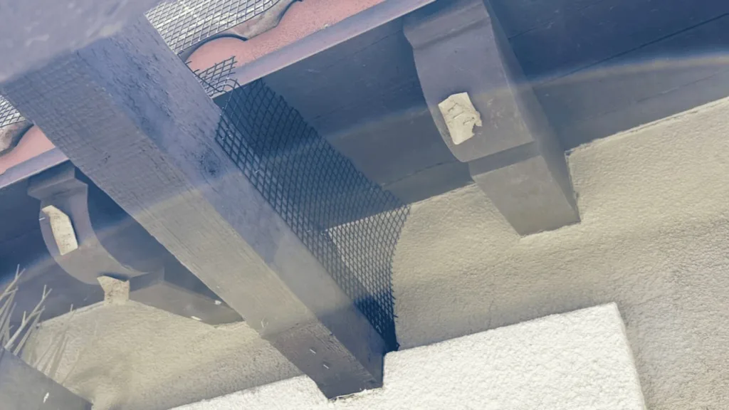 Underneath a concrete balcony/beam with a metal mesh guard and a small chipped patch on the pillar surface