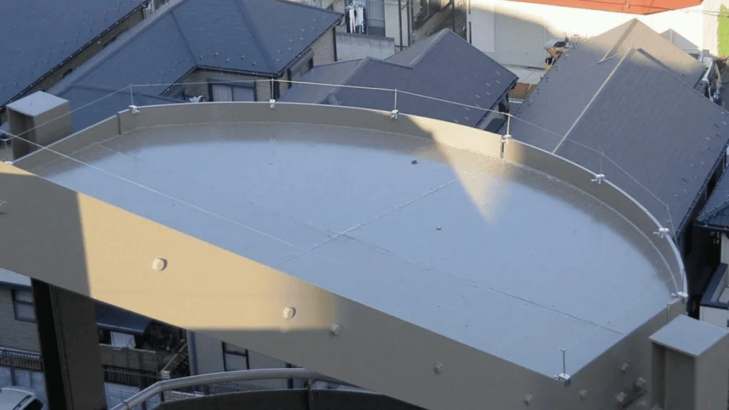 Circular metal rooftop deck with a railing and tension cables, seen over neighboring gray-tiled buildings.