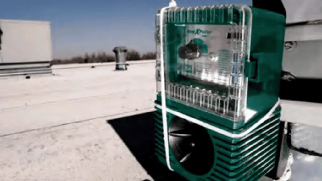 Green rooftop HVAC unit with metal grille on a sunny flat roof against a blue sky.