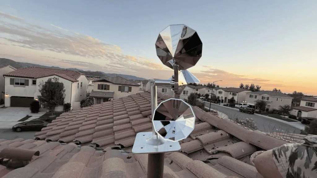 Reflective, multi-faced rooftop antenna mounted on a tile roof overlooking a suburban street at sunset.