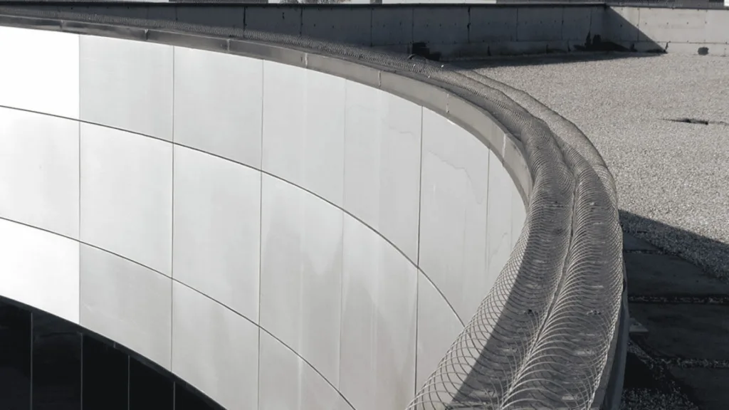 Curved white tiled building wall with a metal mesh railing along the roof edge as a safety barrier on a rooftop.