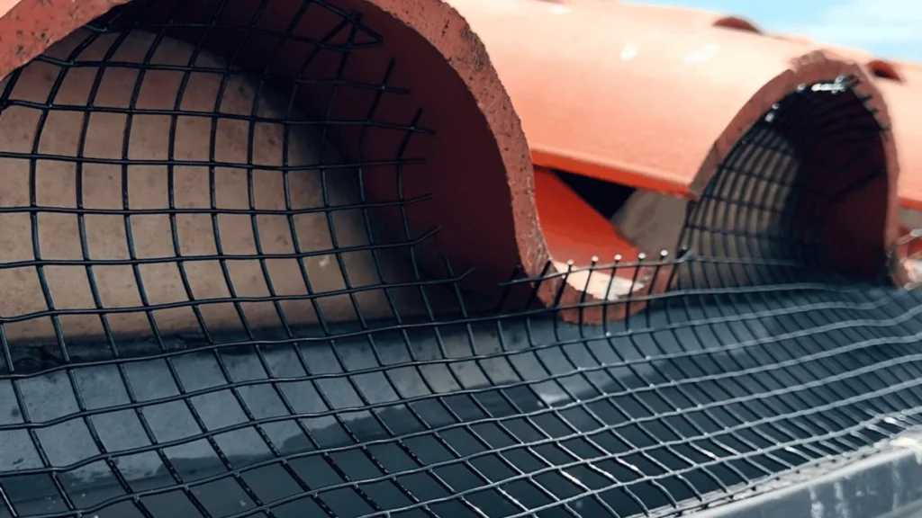 Close-up of a curved metal wire mesh over an orange industrial duct or barrel.