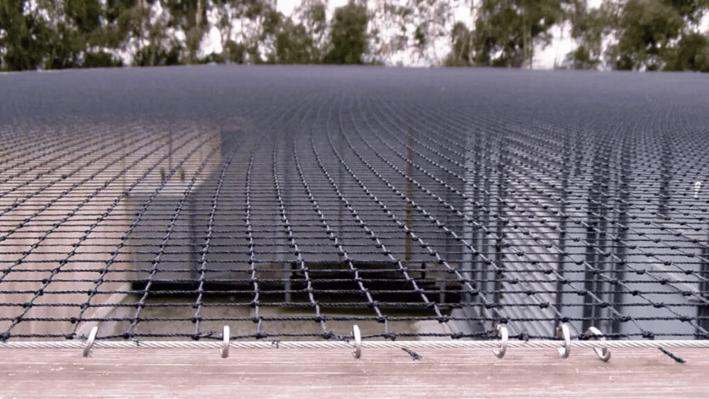 Close-up of a chain-link fence with barbed wire along a rooftop, trees in the background