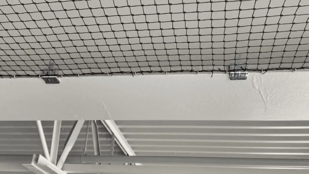Underside of a metal wire-mesh ceiling grid with supporting brackets in an industrial space.