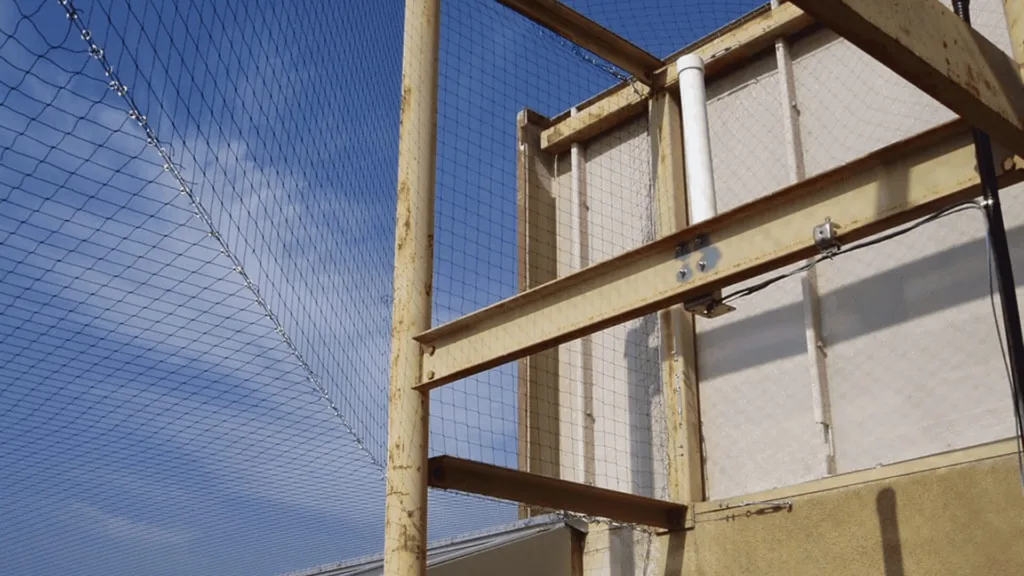Rusty yellow metal framework and chain-link fence enclosing an industrial building against a clear blue sky.