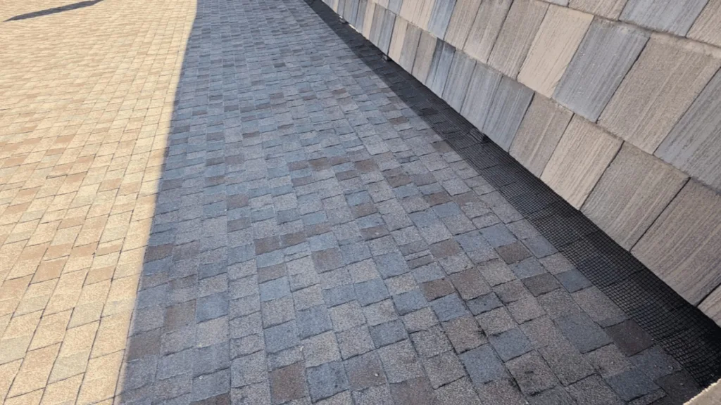 Two-tone brick walkway (tan on the left, blue-gray in the center) beside a stone-clad wall, with a metal drainage grate along the base.