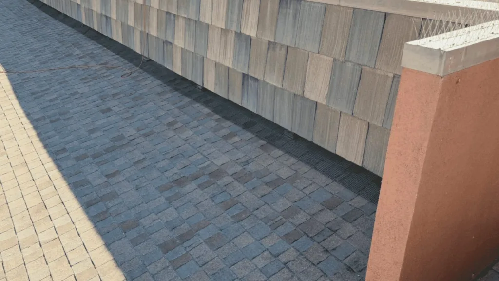 Outdoor walkway beside a stacked-stone wall, with blue-gray paving and a rope lying on the ground.