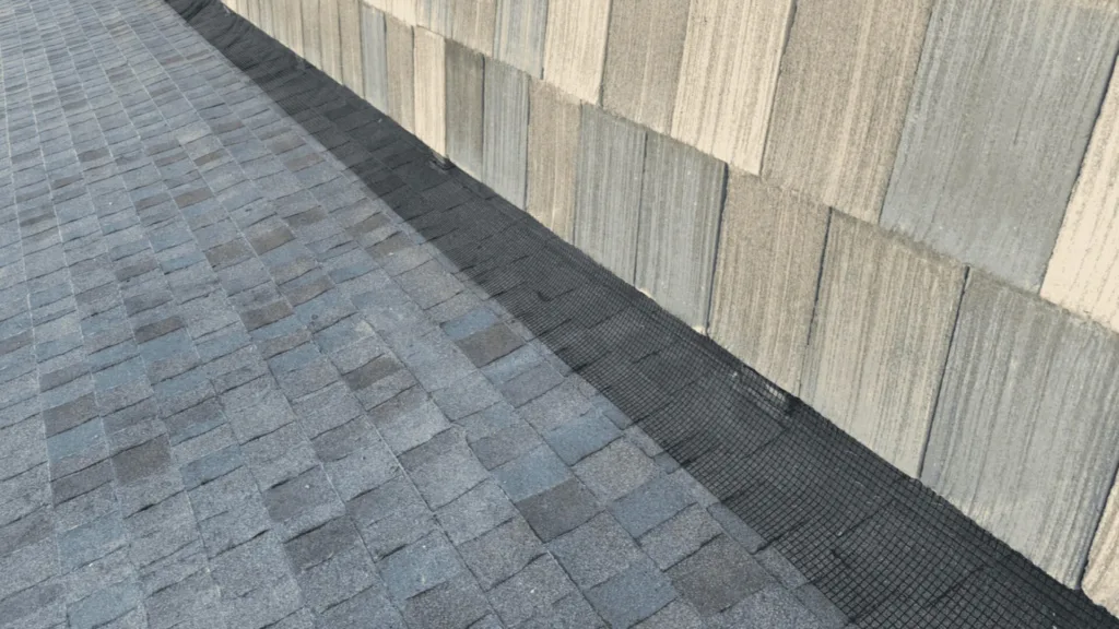 Close-up of a sloped roof with gray asphalt shingles and a black waterproofing mesh along a roof seam.