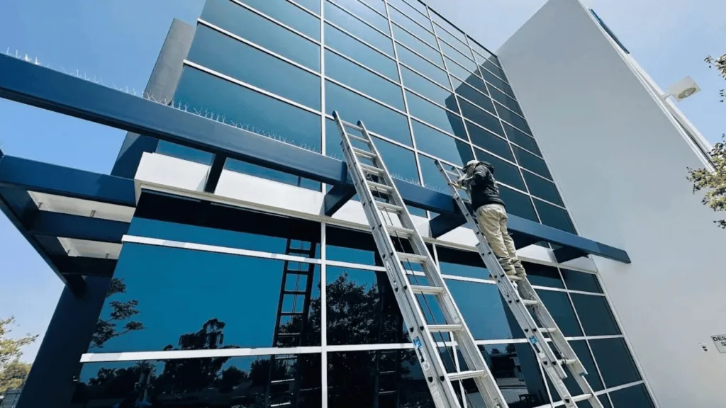 Construction worker on a tall ladder inspecting the glass-fronted building facade.