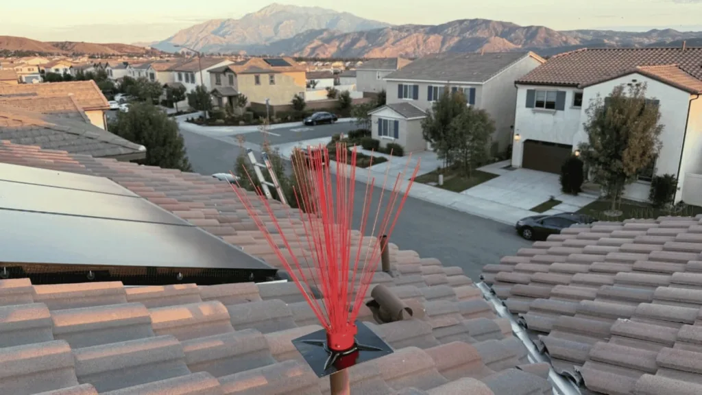 Red radial rooftop antenna mounted on a tile roof overlooking a suburban street with mountains in the distance.