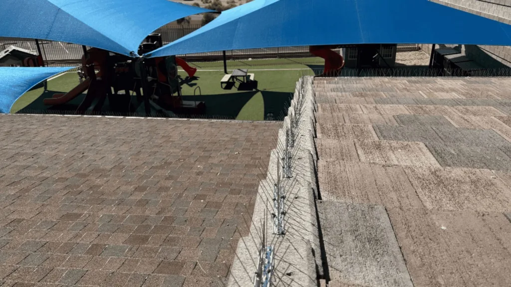 Rooftop playground under large blue shade sails, with slides and play structures on artificial turf visible below the shade.