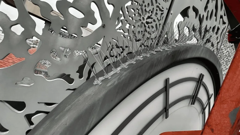 Close-up of a bicycle wheel with a white tire, surrounded by a gray perforated metal decorative panel and an orange background.