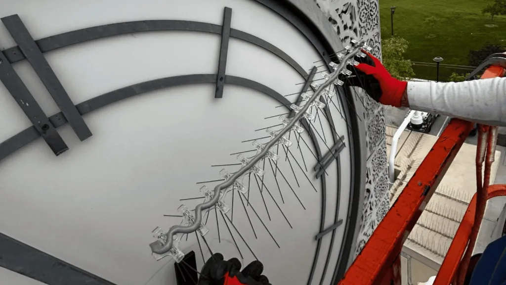 Worker in red gloves secures a cable along the edge of a large circular metallic structure on a scaffold.