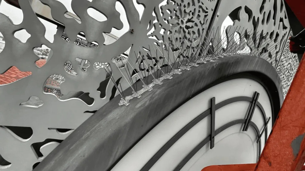 Close-up of a bicycle wheel with a perforated, sculptural metal panel and taut spokes, set against a red frame.