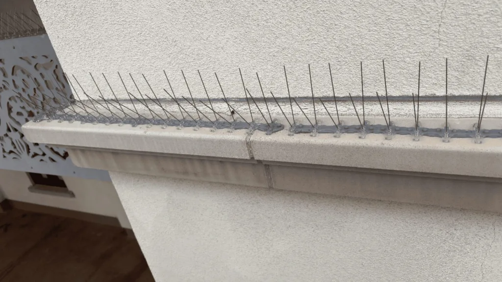 Barbed razor wire runs along a concrete ledge outside a building, with a decorative metal panel on the left.