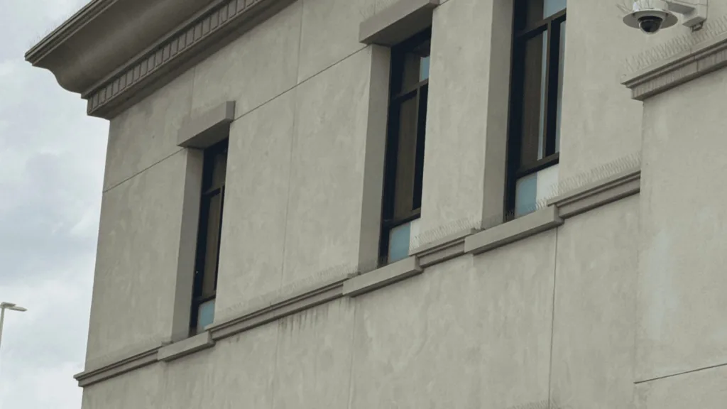 Beige concrete building facade with tall rectangular windows and a decorative cornice.