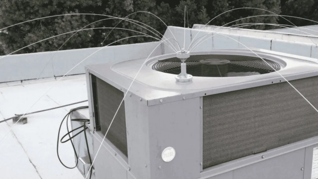 Roof-mounted HVAC condenser with exposed fan and wiring on a white rooftop; trees in the background