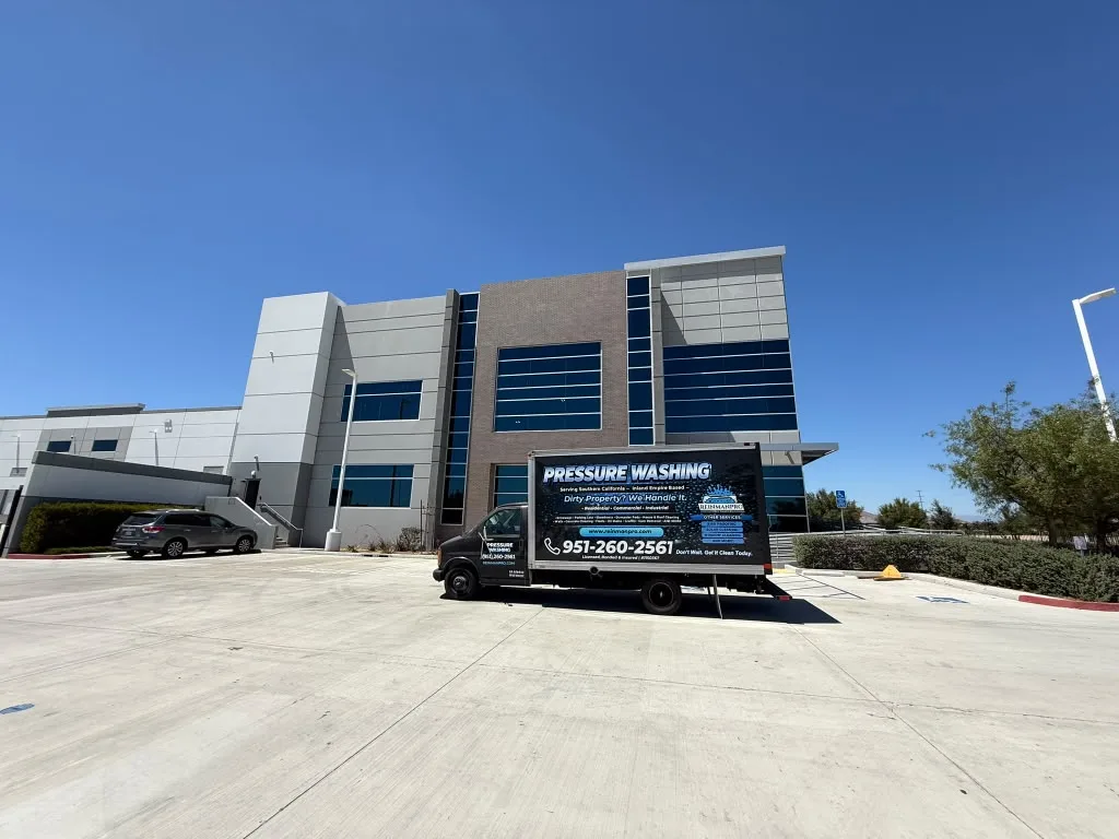 Modern office building with glass windows and brick accents on a sunny day; a pressure-washing truck parked in front.