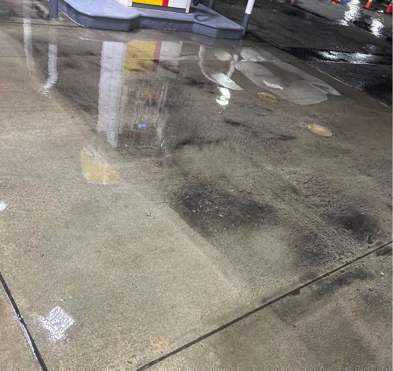 Wet concrete at a gas station, with puddles reflecting the pump island and surrounding lights.
