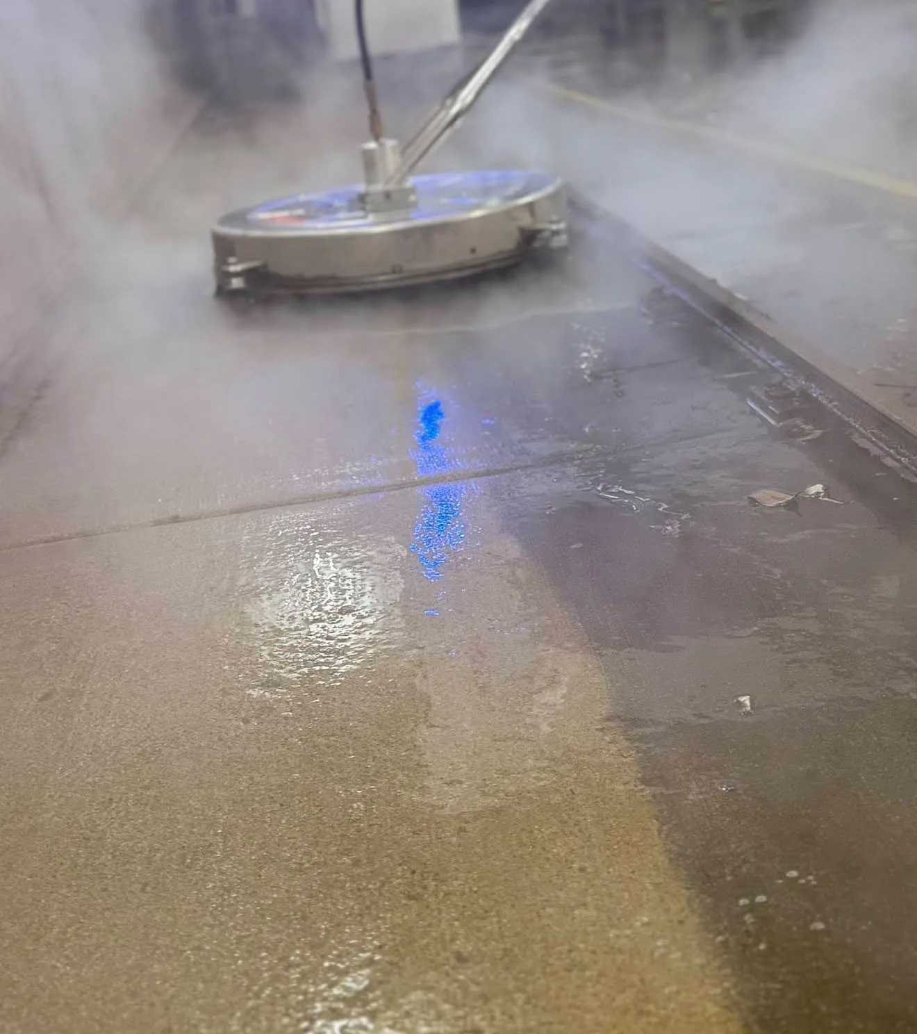 Floor polishing machine moving across a wet, reflective concrete floor with steam.